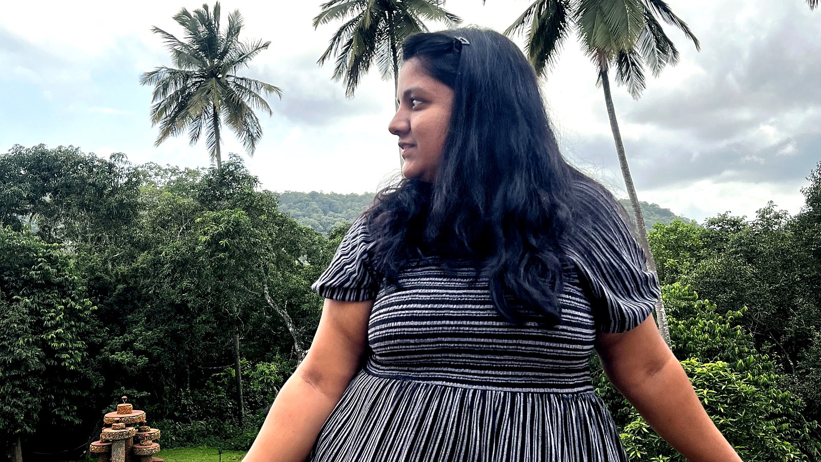 Arthi Rajendran in profile among palm trees, wearing a black and white striped dress