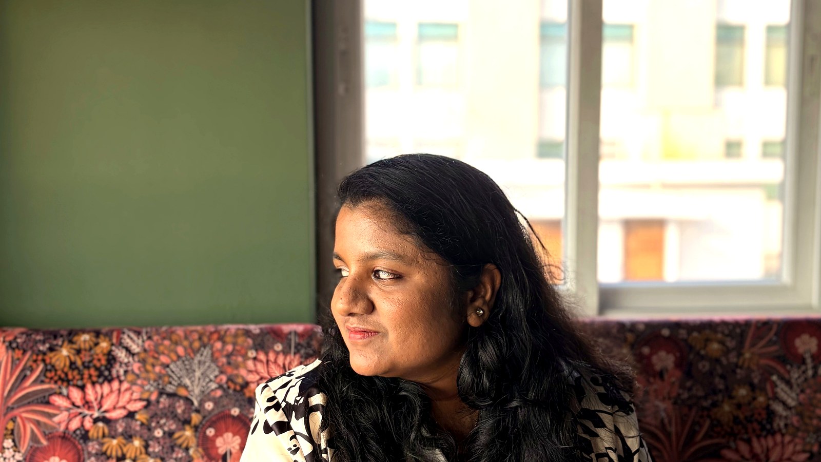 Arthi Rajendran looking aside with a slight smile beside a bright window