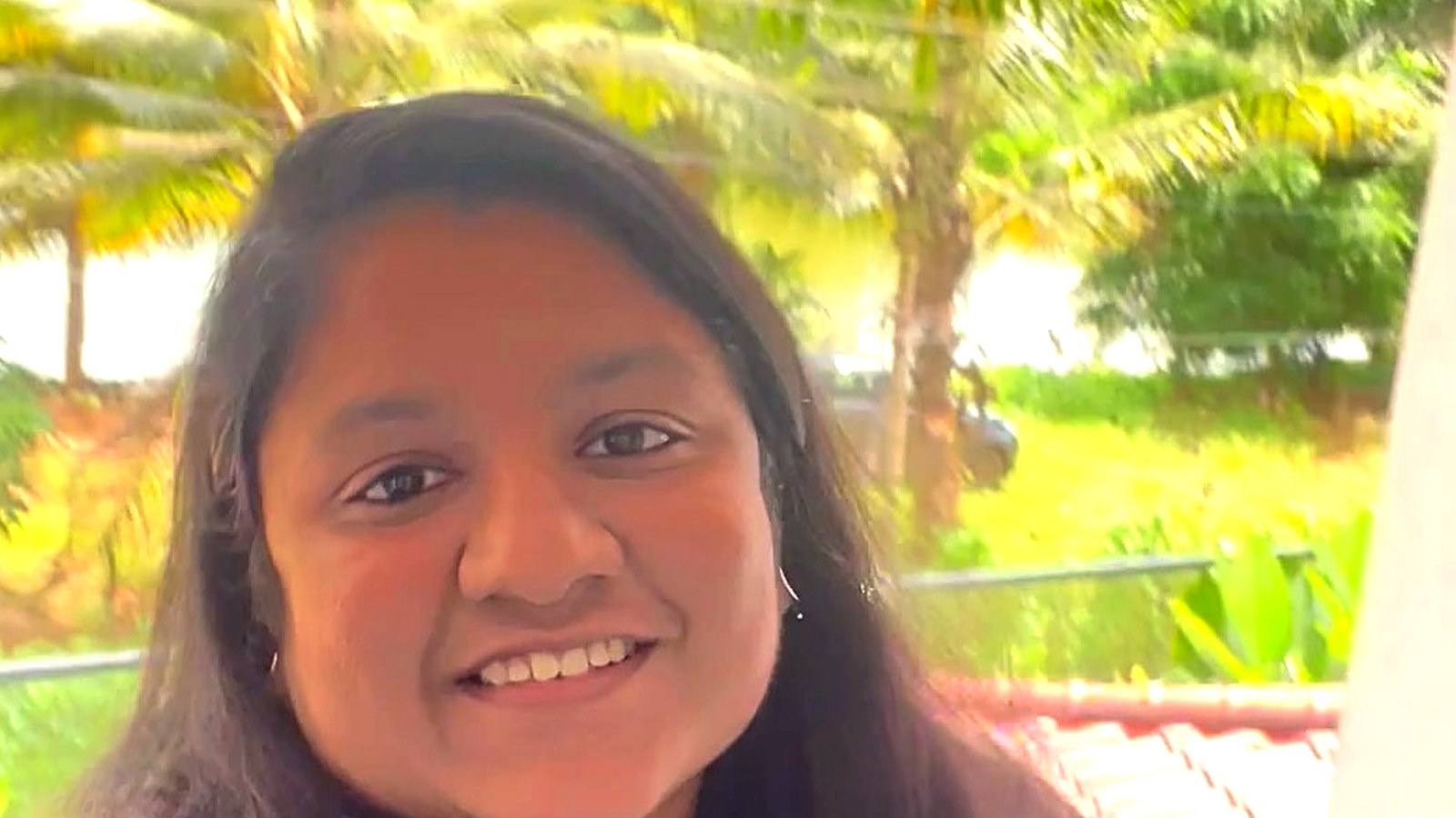 Arthi Rajendran smiling at the camera outdoors, with palm trees behind her