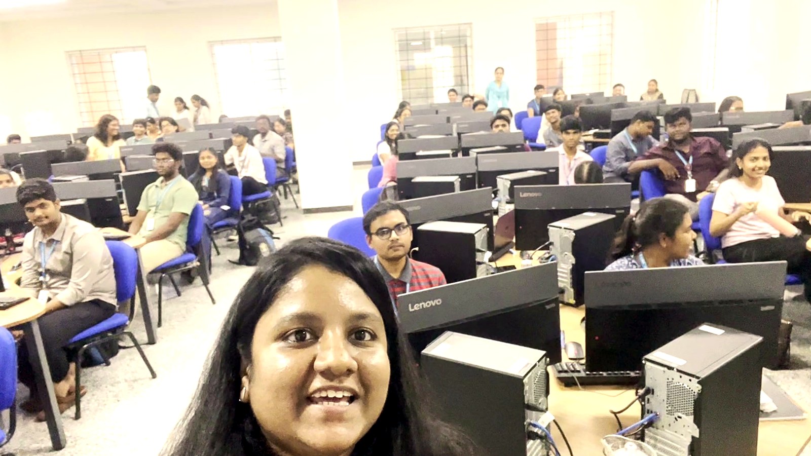 Arthi Rajendran smiling at the camera in a computer lab, with students seated behind her